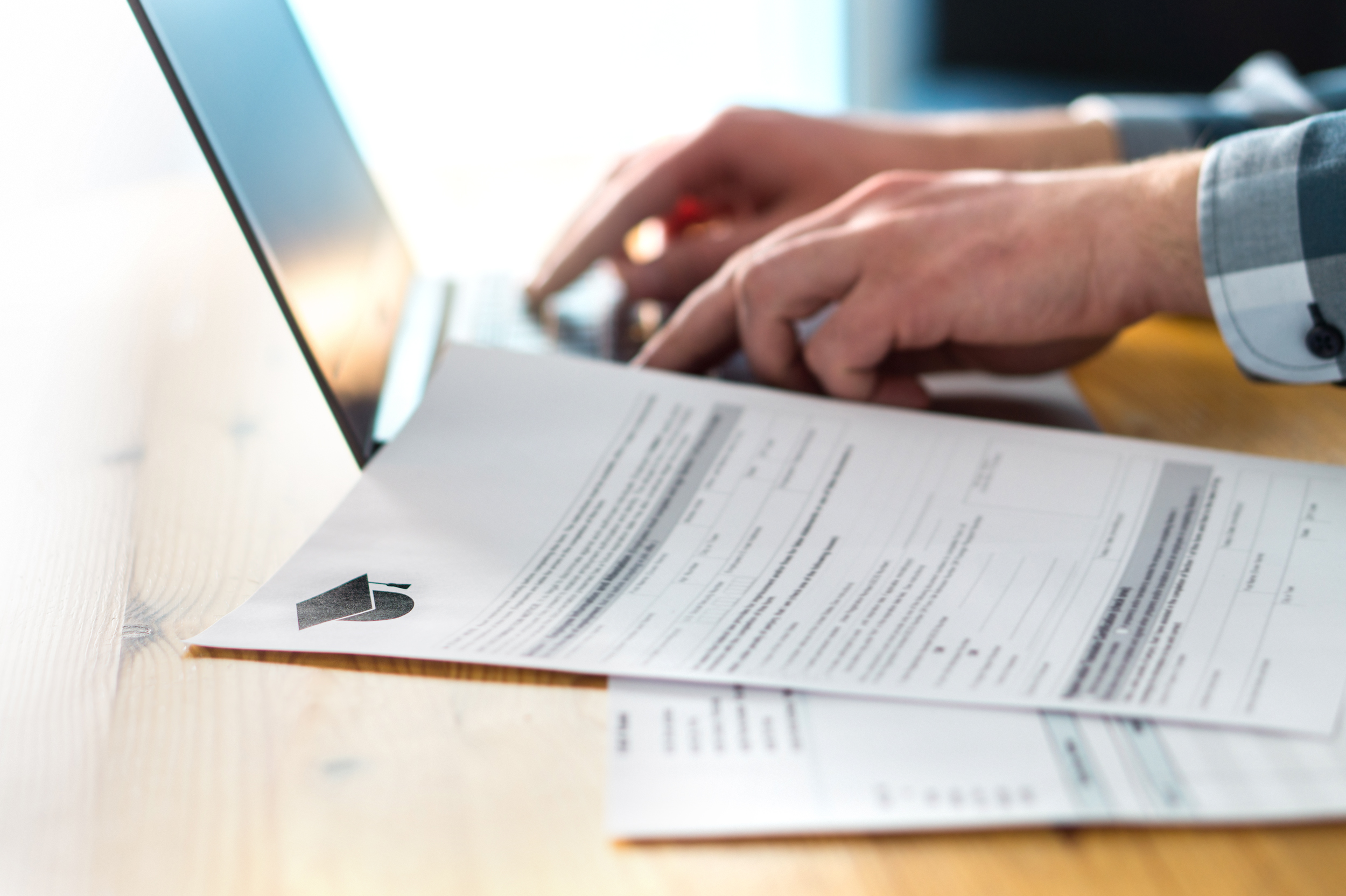 Young man writing college or university application form with laptop. Student applying to school. Scholarship document, admission paper or letter on table. Typing email.